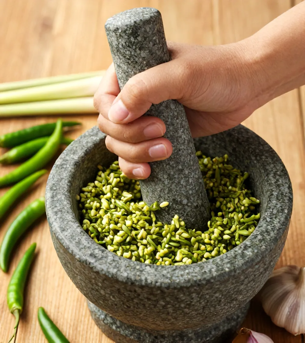 Hands pounding green curry paste in a granite mortar
